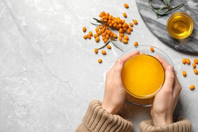 Woman holding cup with sea buckthorn tea at grey table, top view. Space for text