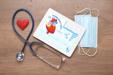 Photo of Flat lay composition with tablet and red heart on wooden table. Cardiology concept