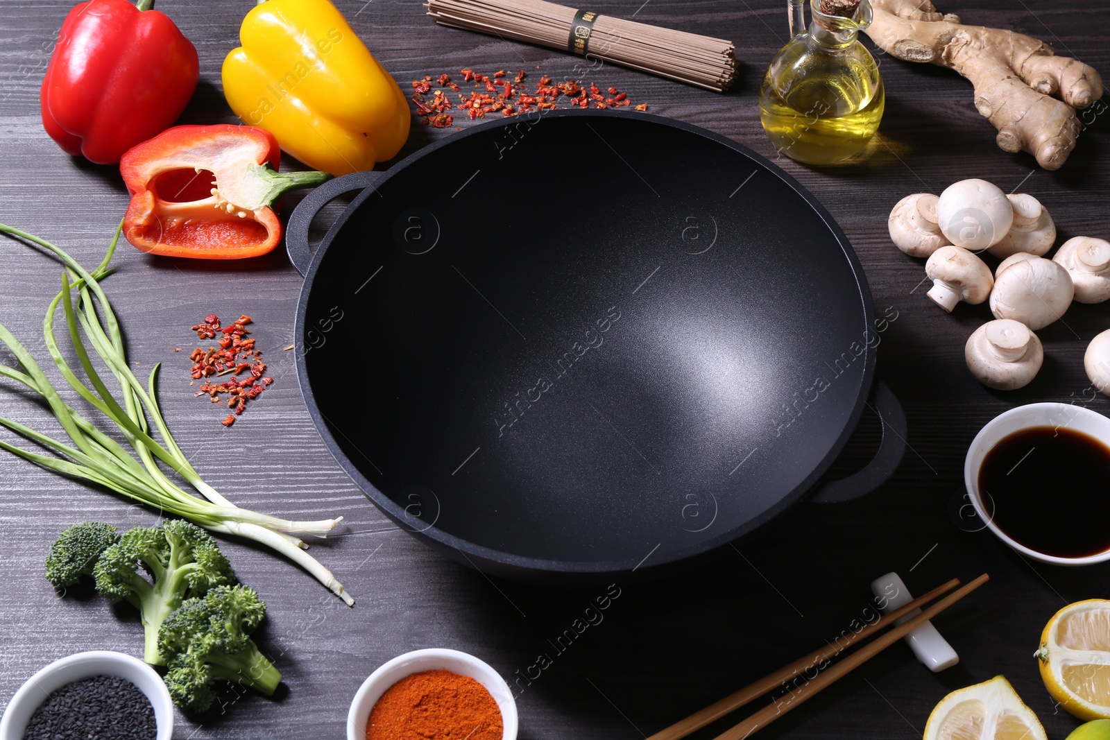 Photo of Empty iron wok and chopsticks surrounded by ingredients on dark grey wooden table