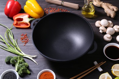 Photo of Empty iron wok and chopsticks surrounded by ingredients on dark grey wooden table