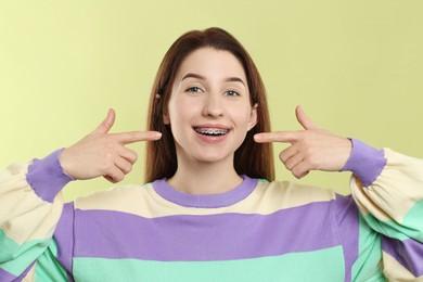 Photo of Portrait of smiling woman pointing at her dental braces on light green background