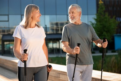 Happy senior couple practicing Nordic walking with poles outdoors on sunny day