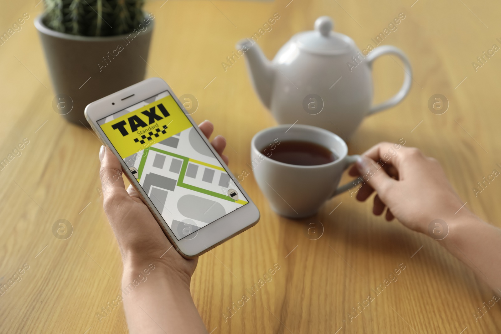 Photo of Woman ordering taxi with smartphone at wooden table, closeup