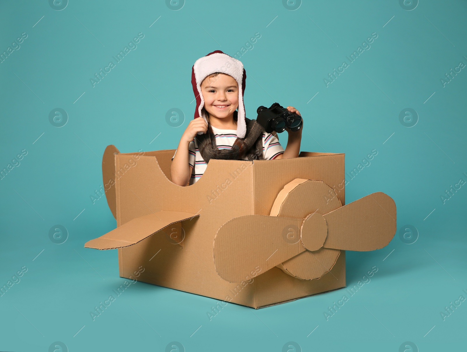 Photo of Cute little boy playing with binoculars and cardboard airplane on color background