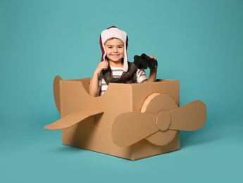 Cute little boy playing with binoculars and cardboard airplane on color background