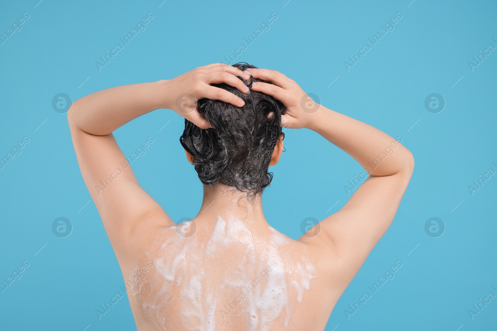 Photo of Woman washing hair on light blue background, back view