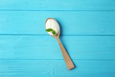 Photo of Spoon of sour cream with basil on light blue wooden table, top view