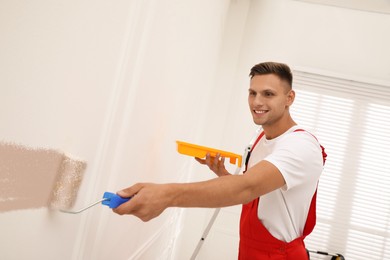 Photo of Worker painting wall with roller on ladder indoors