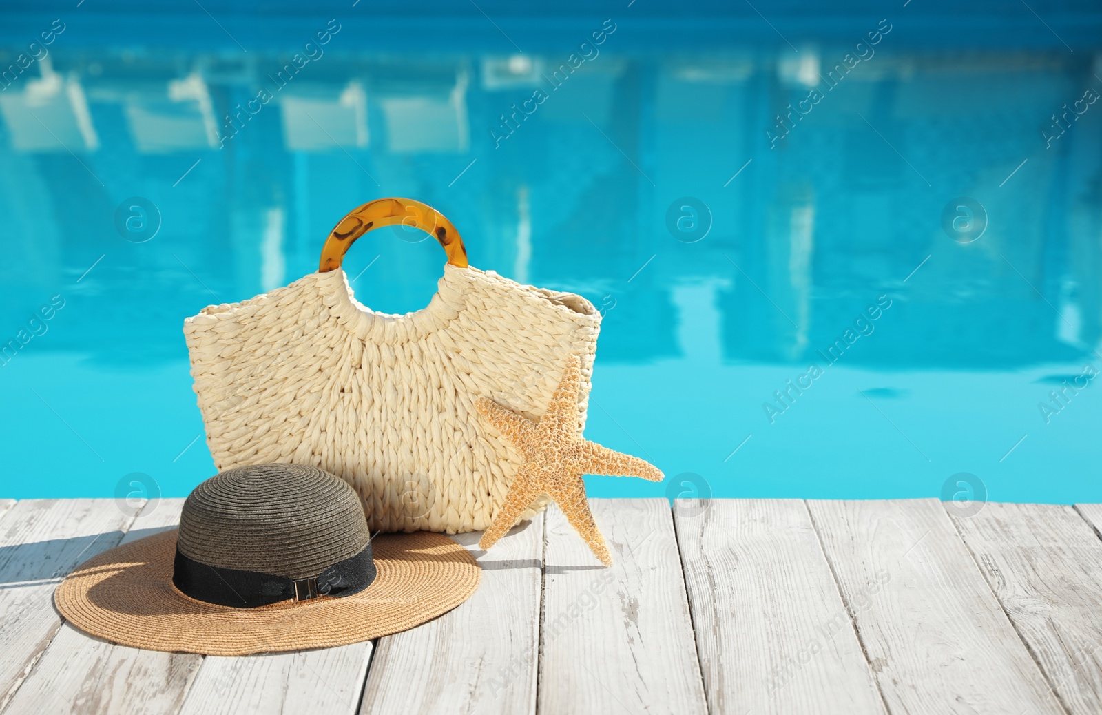 Photo of Beach accessories on wooden deck near outdoor swimming pool, space for text