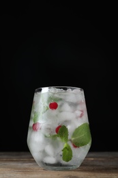 Photo of Vodka cocktail with cranberries and ice on wooden table against black background. Space for text