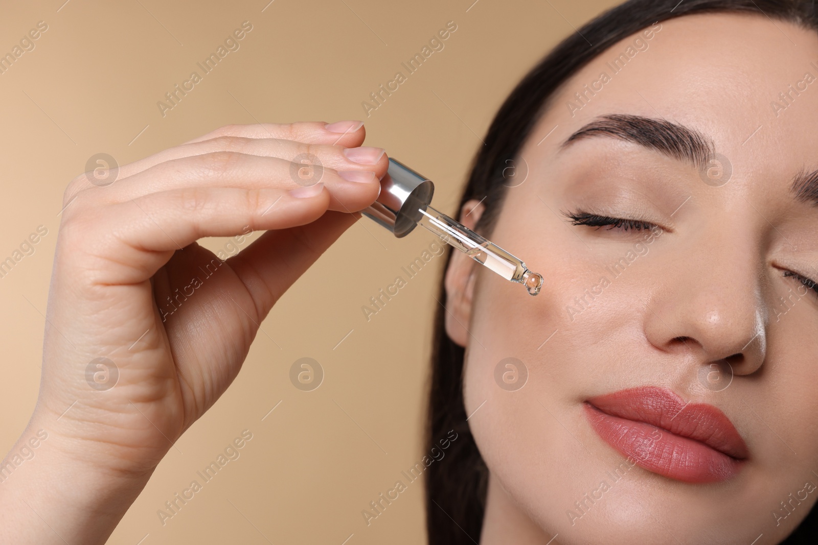 Photo of Young woman applying essential oil onto face on beige background, closeup