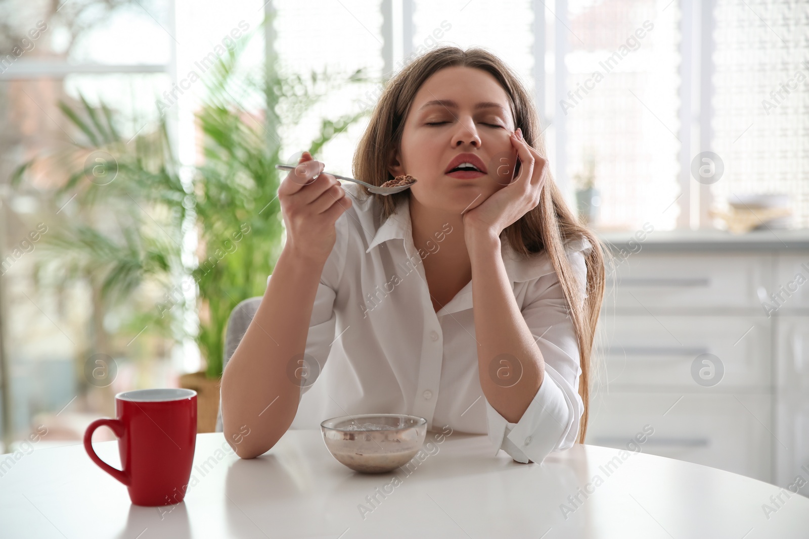 Photo of Sleepy young woman eating breakfast at home in morning