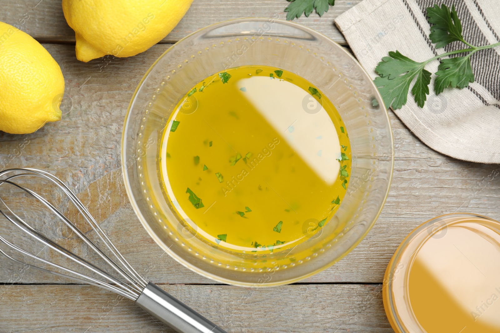 Photo of Bowl with lemon sauce and ingredients on wooden table, flat lay. Delicious salad dressing