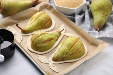 Photo of Tray with raw dough and fresh pears on white table, closeup