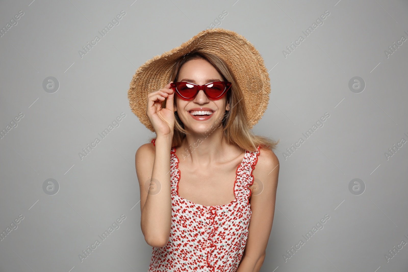 Photo of Beautiful young woman wearing straw hat and sunglasses on light grey background. Stylish headdress