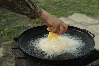 Photo of Man cooking delicious potato wedges on frying pan outdoors, closeup