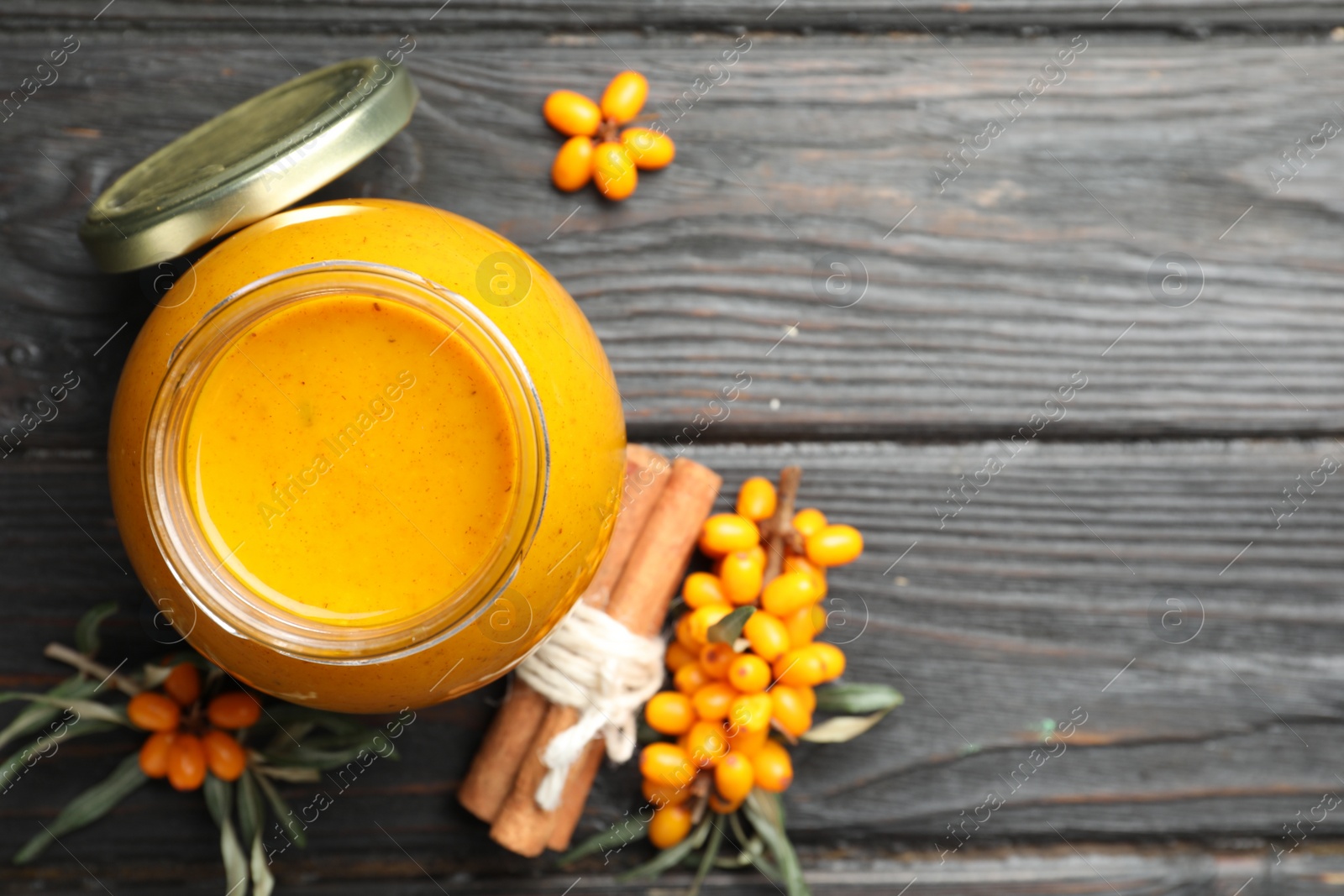 Photo of Delicious sea buckthorn jam and fresh berries on black wooden table, flat lay. Space for text