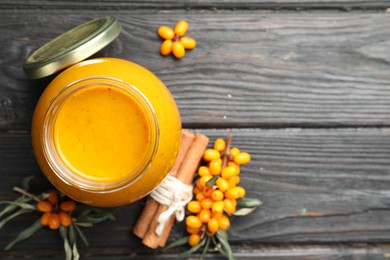 Photo of Delicious sea buckthorn jam and fresh berries on black wooden table, flat lay. Space for text