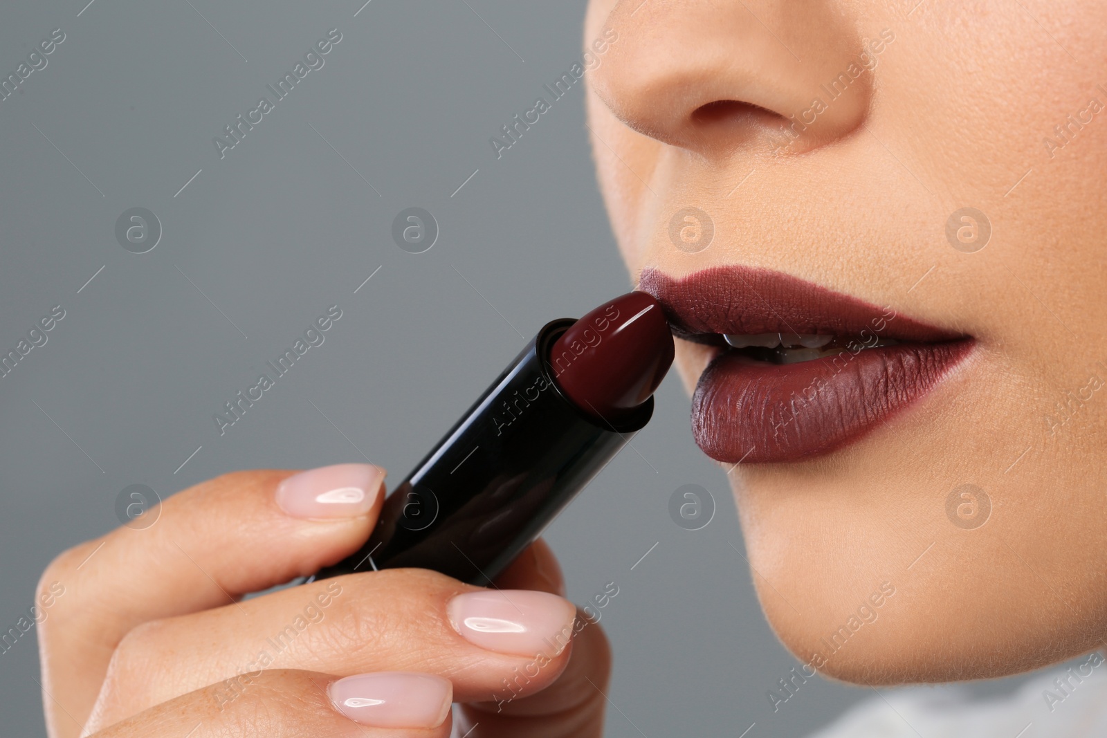 Photo of Beautiful woman applying dark lipstick on gray background, closeup