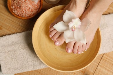 Photo of Woman soaking her feet in bowl with water and flower, top view. Pedicure procedure