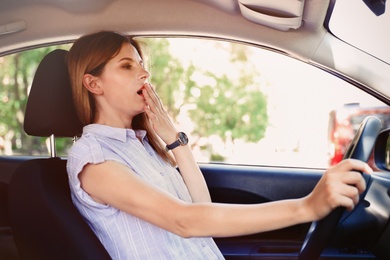 Photo of Tired woman yawning inside car. Unsafe driving