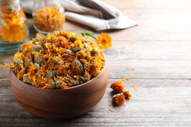 Bowl of dry calendula flowers on wooden table. Space for text