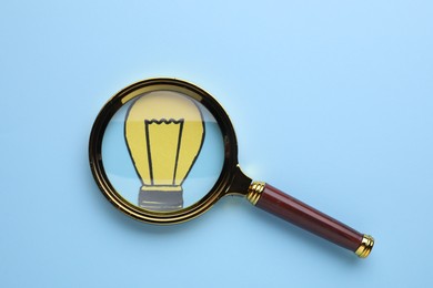 Photo of Magnifying glass over paper light bulb on blue background, top view
