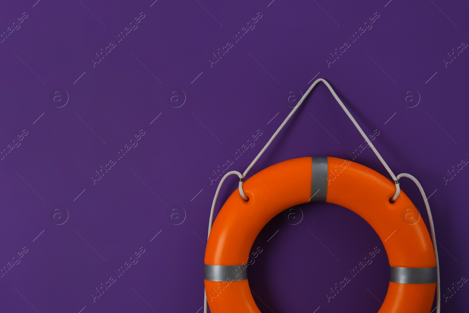 Photo of Orange lifebuoy and space for text on violet background. Rescue equipment