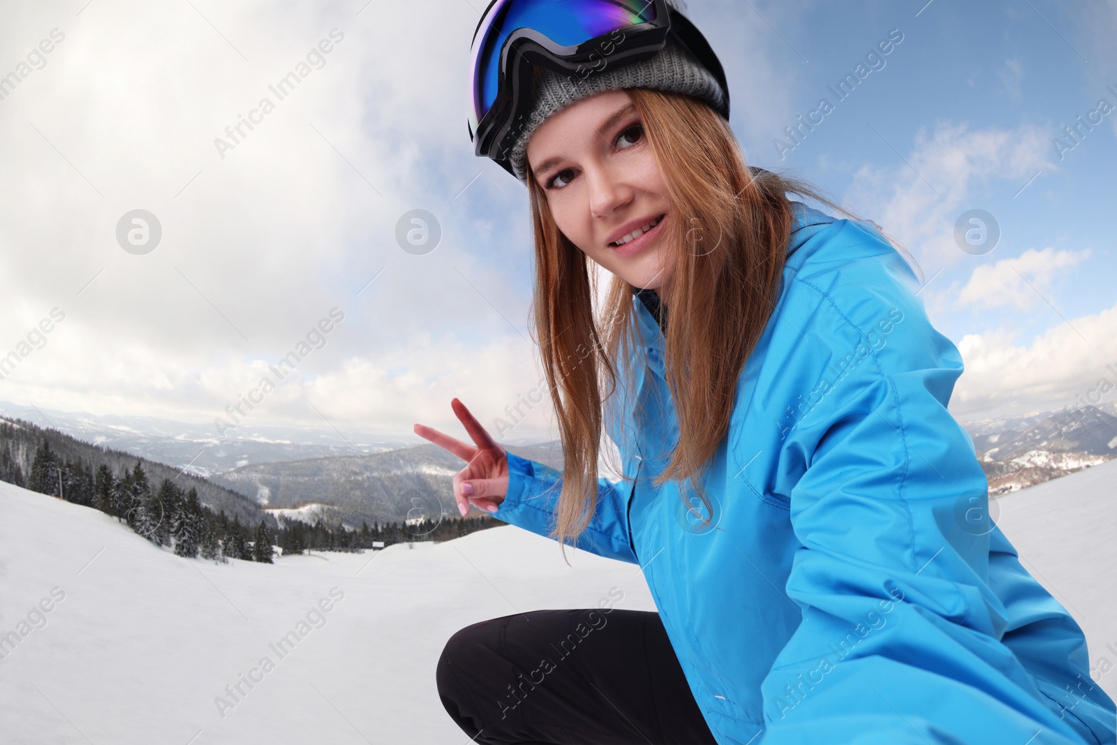 Image of Smiling woman with ski goggles taking selfie in snowy mountains