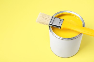 Photo of Can of paint with brush on pale yellow background, closeup. Space for text