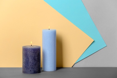 Photo of Decorative wax candles on table against color background