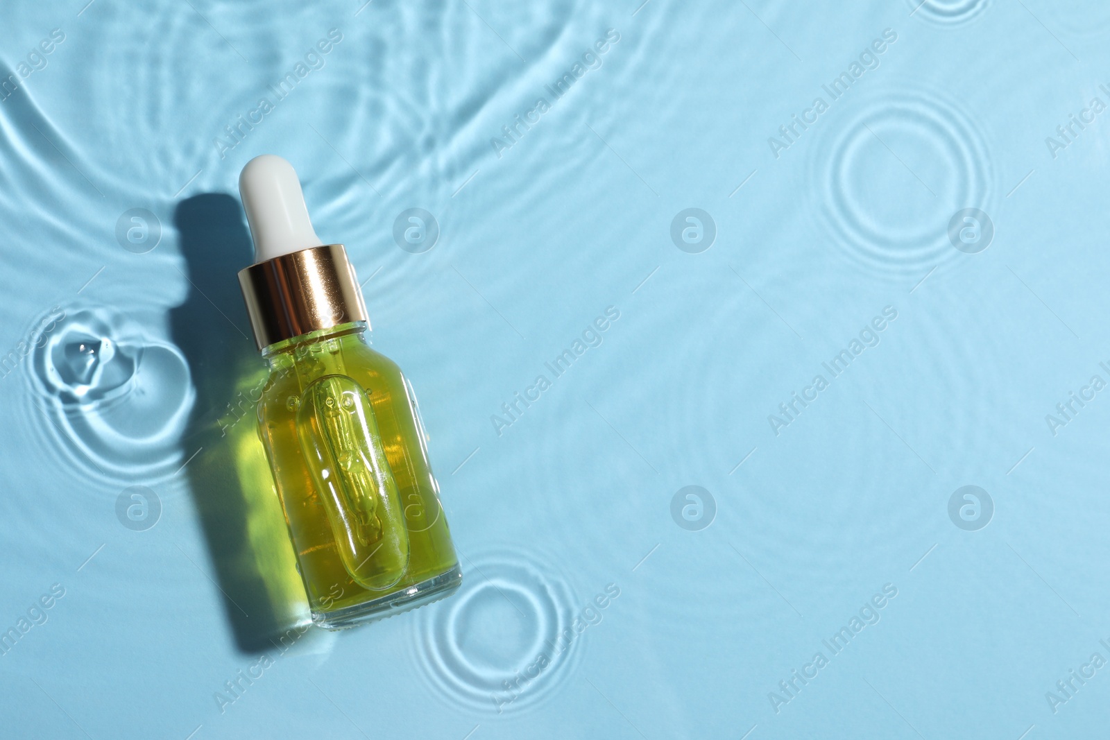 Photo of Bottle of cosmetic oil in water on light blue background, top view. Space for text
