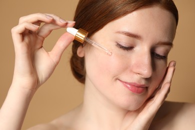 Photo of Beautiful woman with freckles applying cosmetic serum onto her face on beige background, closeup