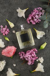 Photo of Bottle of luxury perfume and floral decor on dark grey table, flat lay