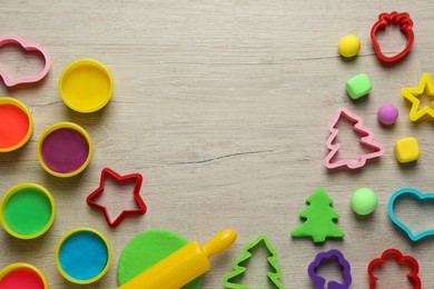 Photo of Different color play dough and tools on wooden table, flat lay. Space for text