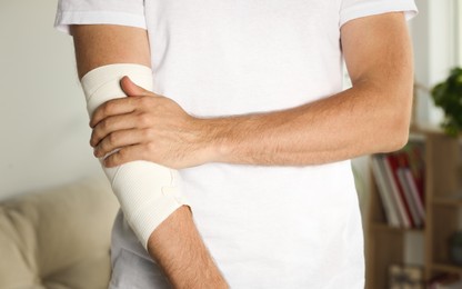 Photo of Man with arm wrapped in medical bandage indoors, closeup