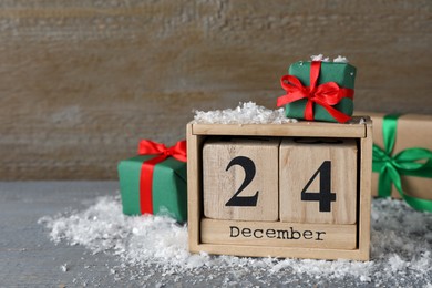 Photo of December 24 - Christmas Eve. Wooden block calendar and gift boxes on grey table, space for text