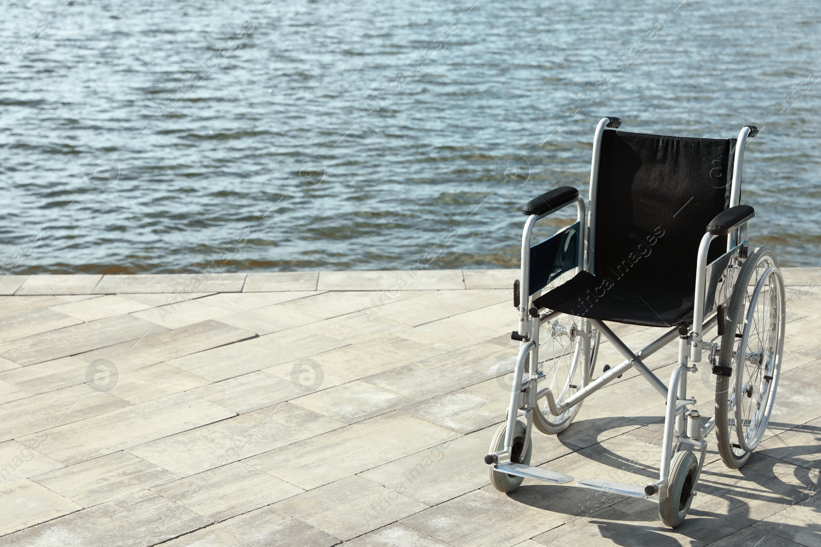 Photo of Empty wheelchair near river on sunny day. Space for text