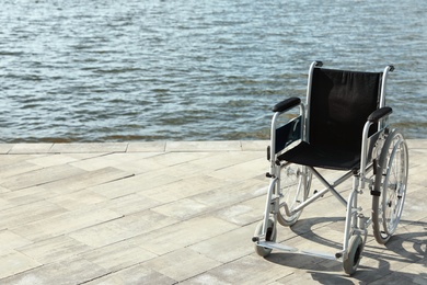 Empty wheelchair near river on sunny day. Space for text