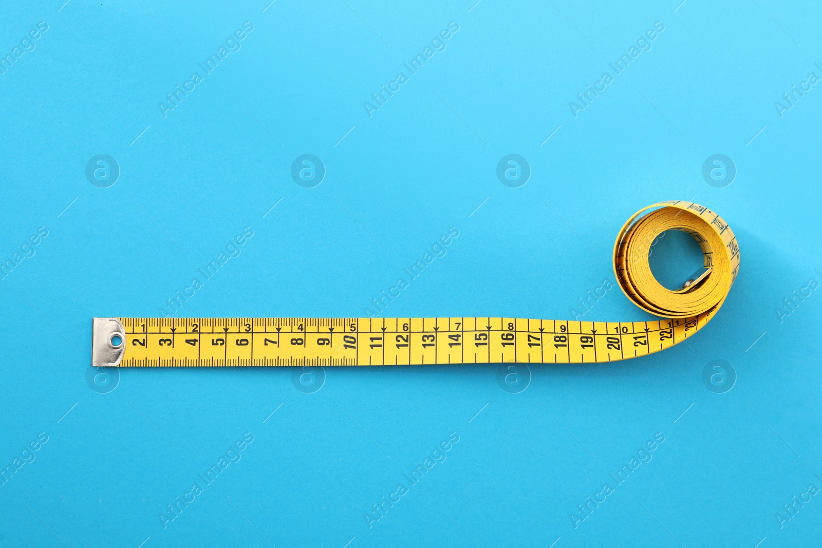 Photo of Yellow measuring tape on light blue background, top view
