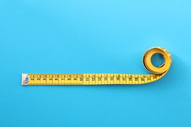 Yellow measuring tape on light blue background, top view