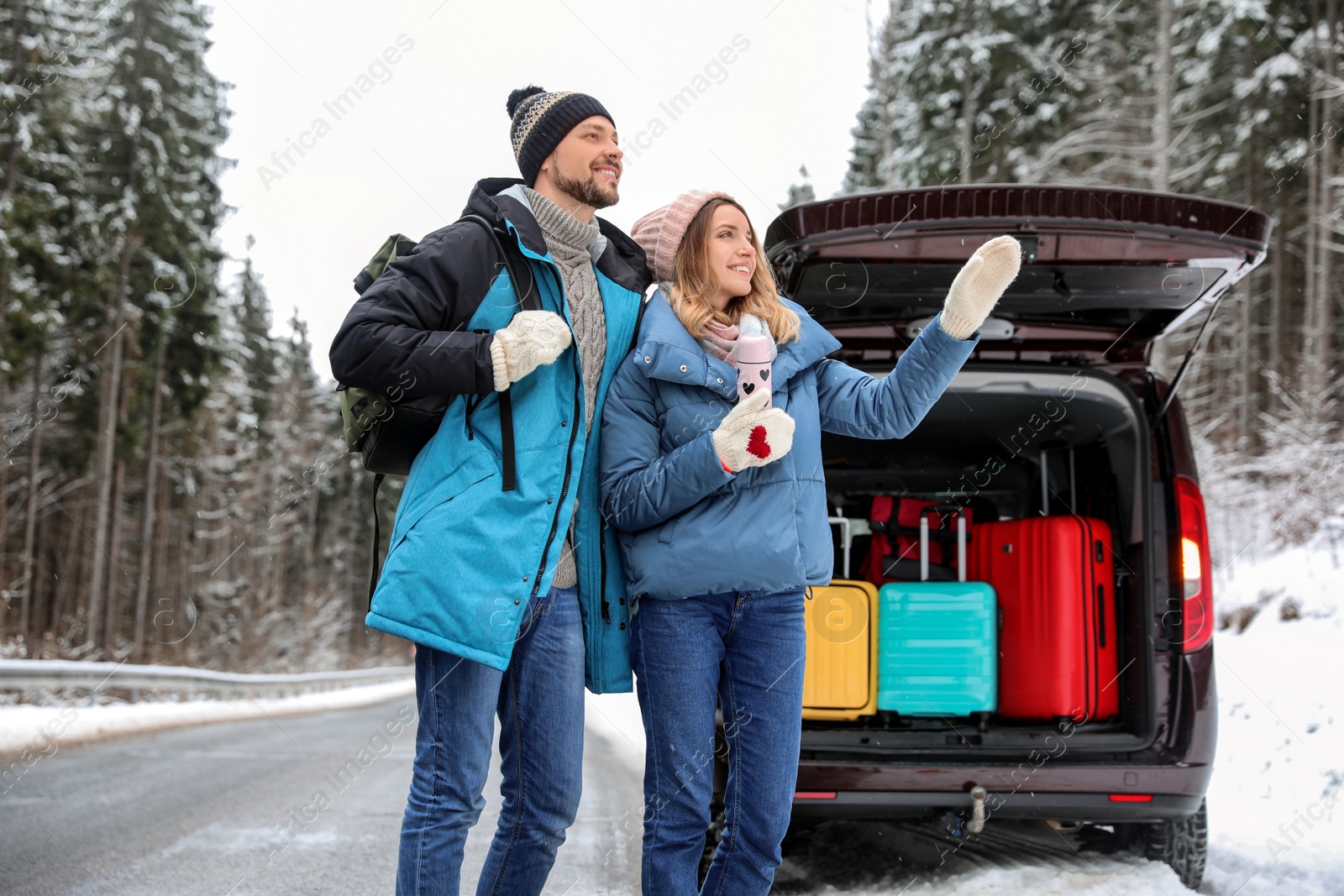 Photo of Couple near open car trunk full of luggage on road. Winter vacation