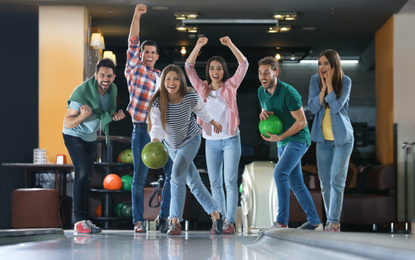 Young woman throwing ball and spending time with friends in bowling club