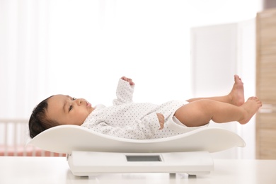 African-American baby lying on scales in light room