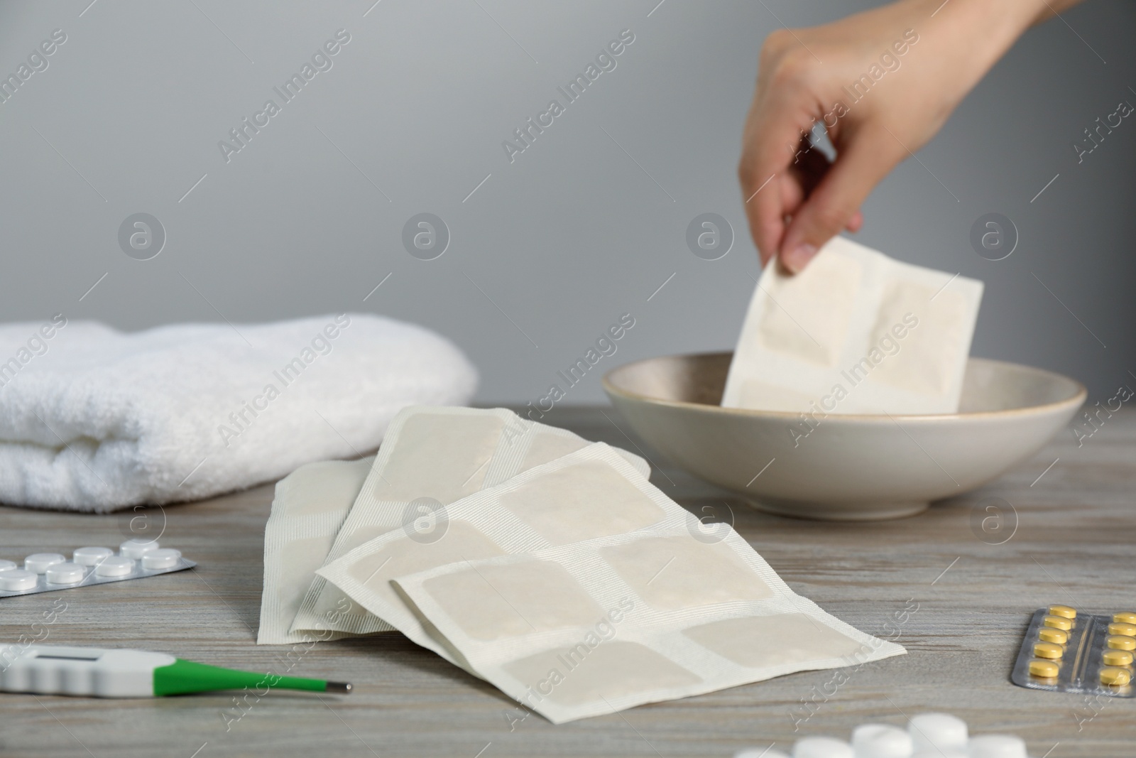 Photo of Woman dipping mustard plaster into bowl with water at wooden table, closeup