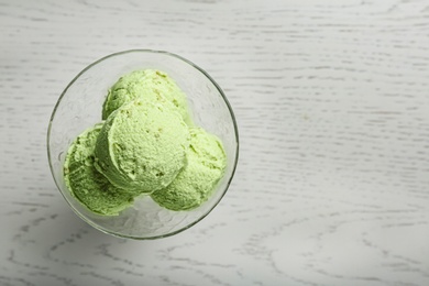 Photo of Delicious green ice cream served in dessert bowl on white wooden table, top view. Space for text