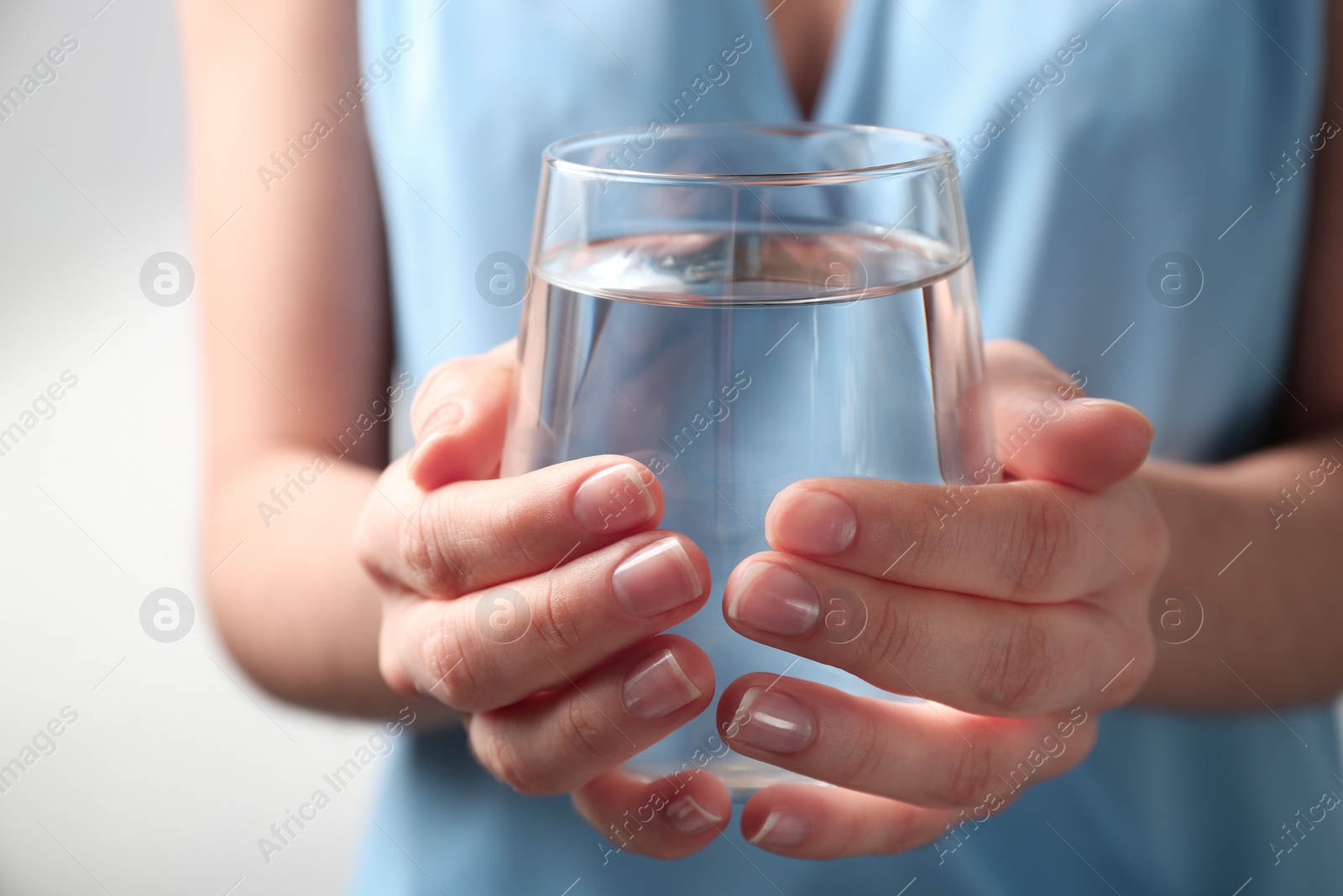 Photo of Woman holding glass with fresh water against light background, closeup