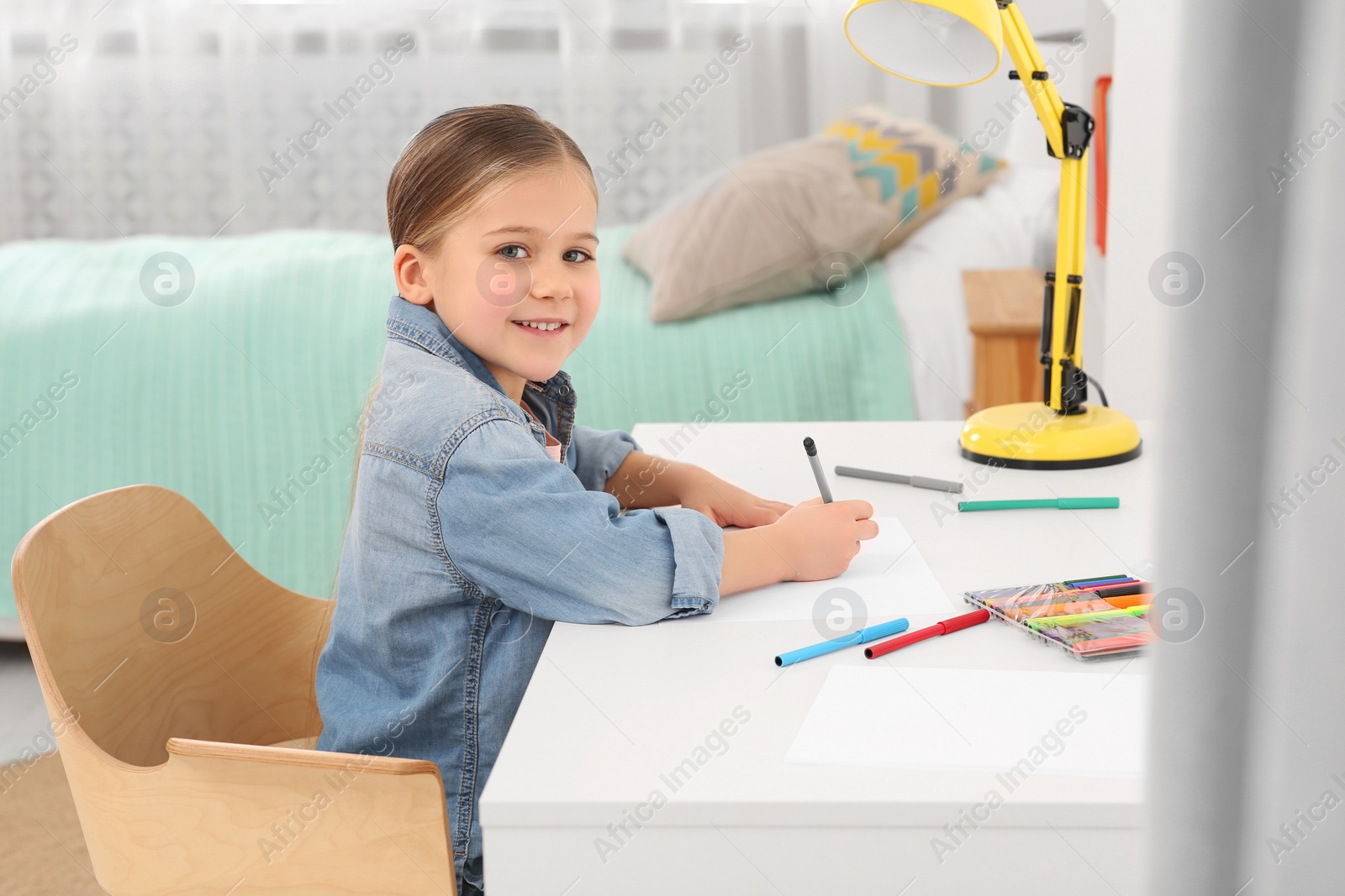 Photo of Cute little girl drawing with markers at desk in room. Home workplace