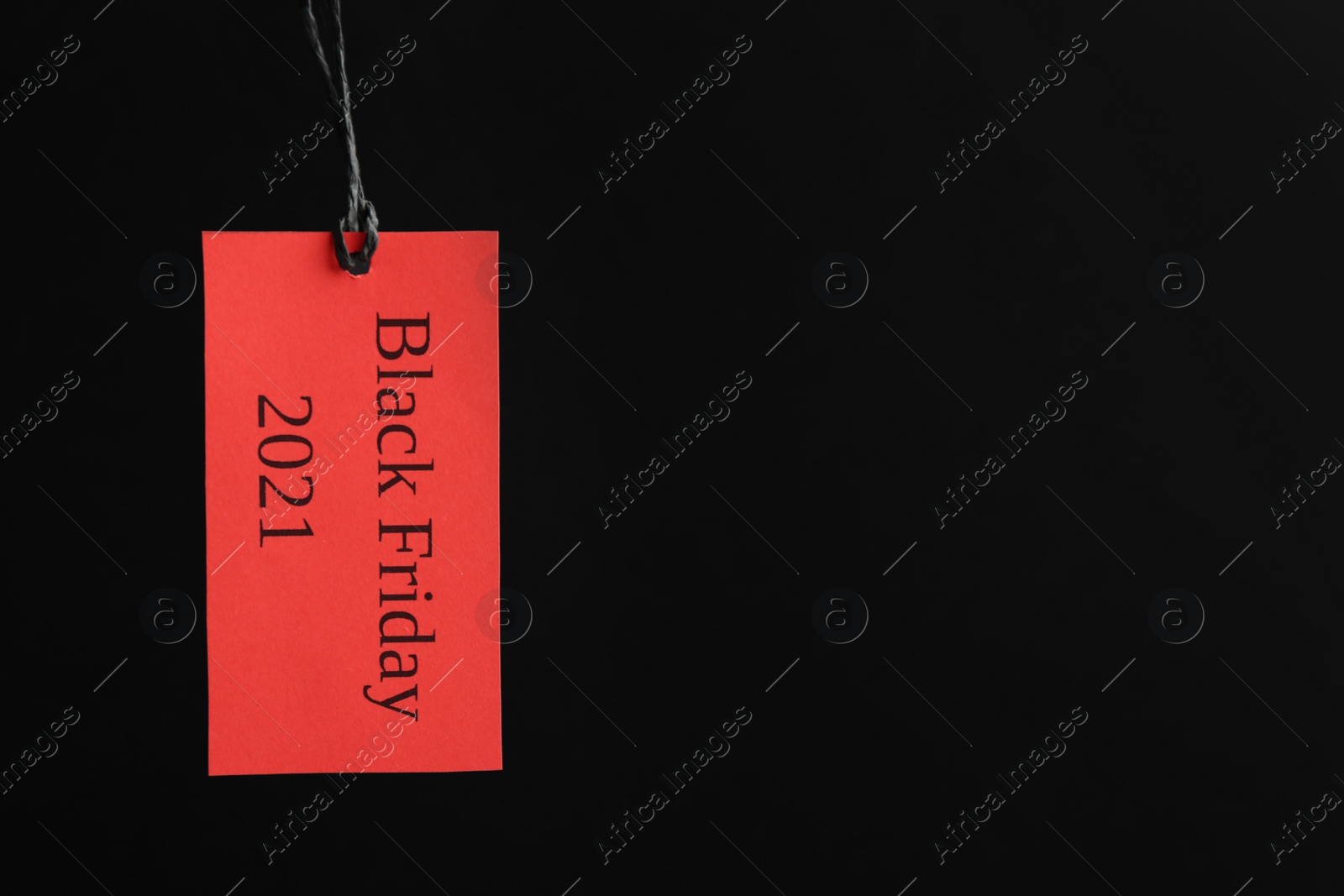 Photo of Red tag with words BLACK FRIDAY 2021 hanging on dark background. Space for text