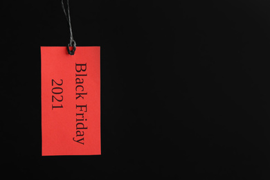 Red tag with words BLACK FRIDAY 2021 hanging on dark background. Space for text